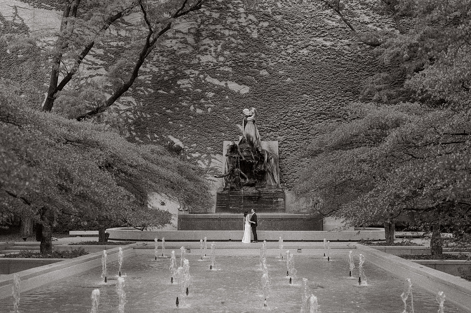 Engaged couples stands in front of the fountain at the Chicago Art Institute Gardens